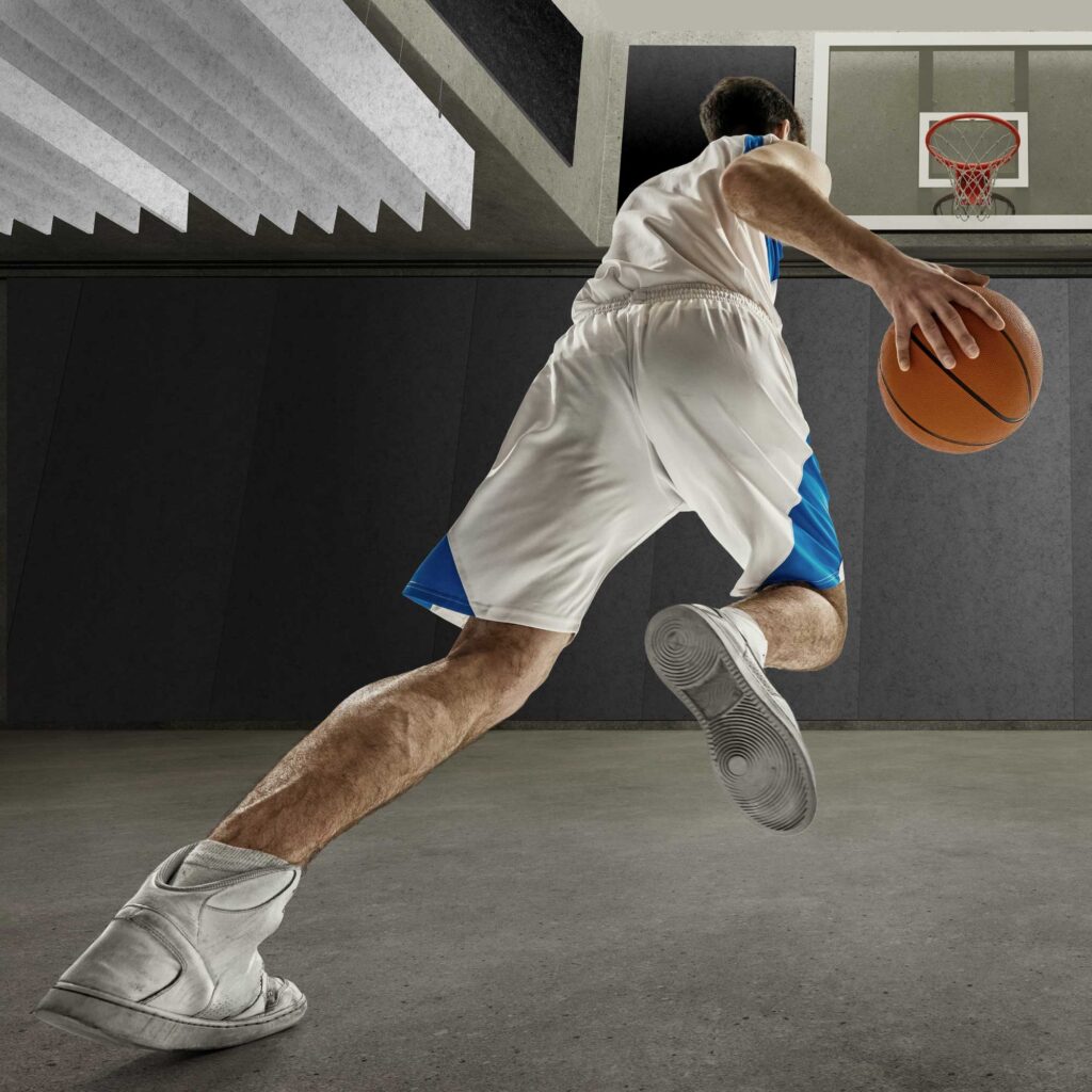Basketball player in gym with High Impact acoustic fins installed on ceiling and High Impact acoustic panels installed on walls